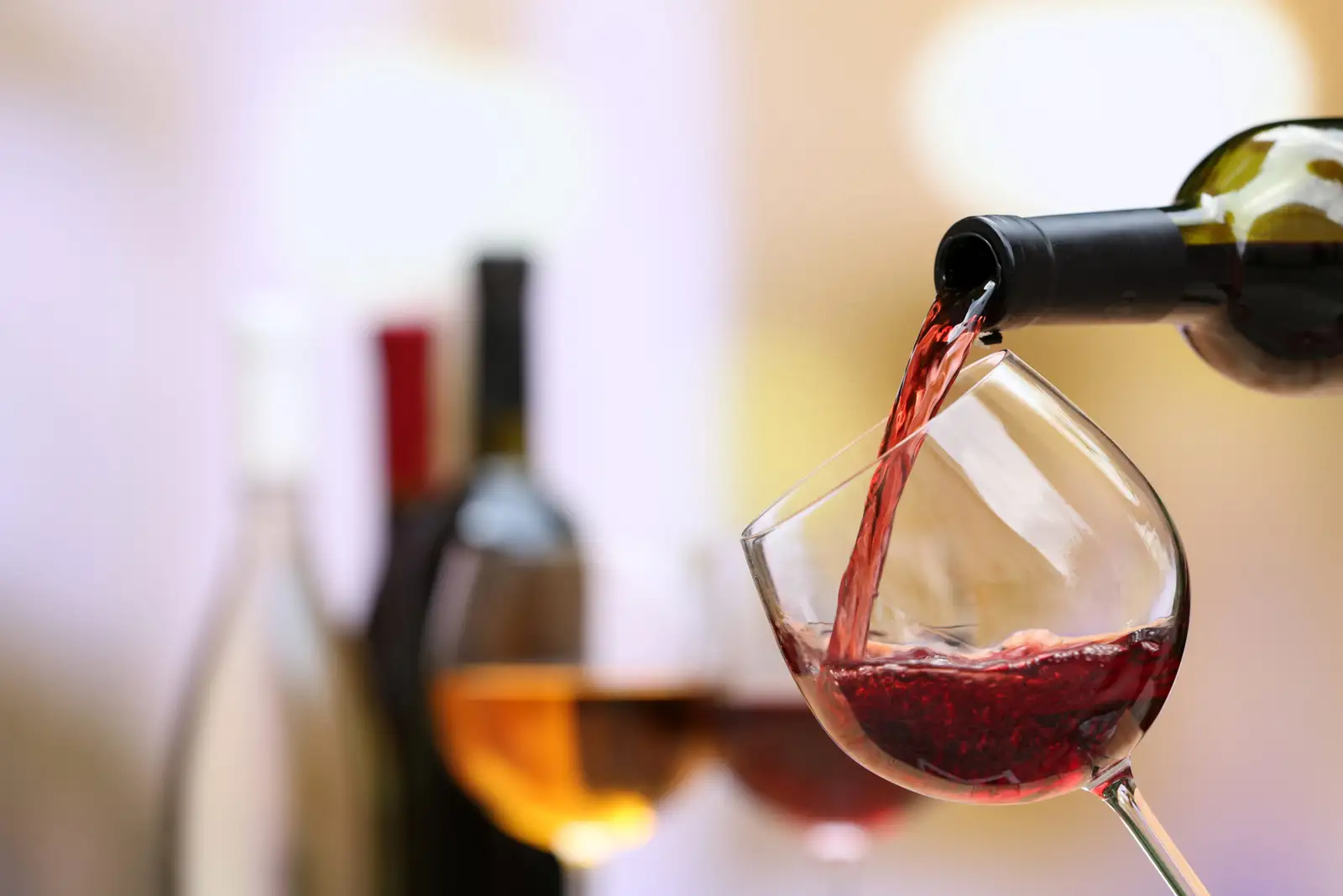 Red wine poured into a glass, with the bottles behind