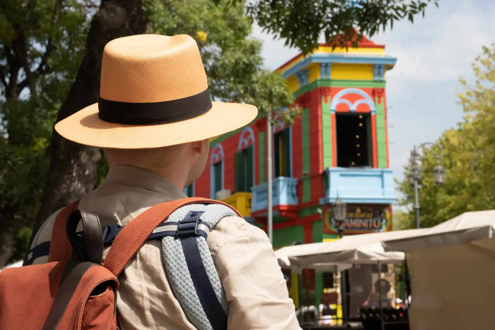 A visitor in a straw hat in front of the painted houses of La Boca