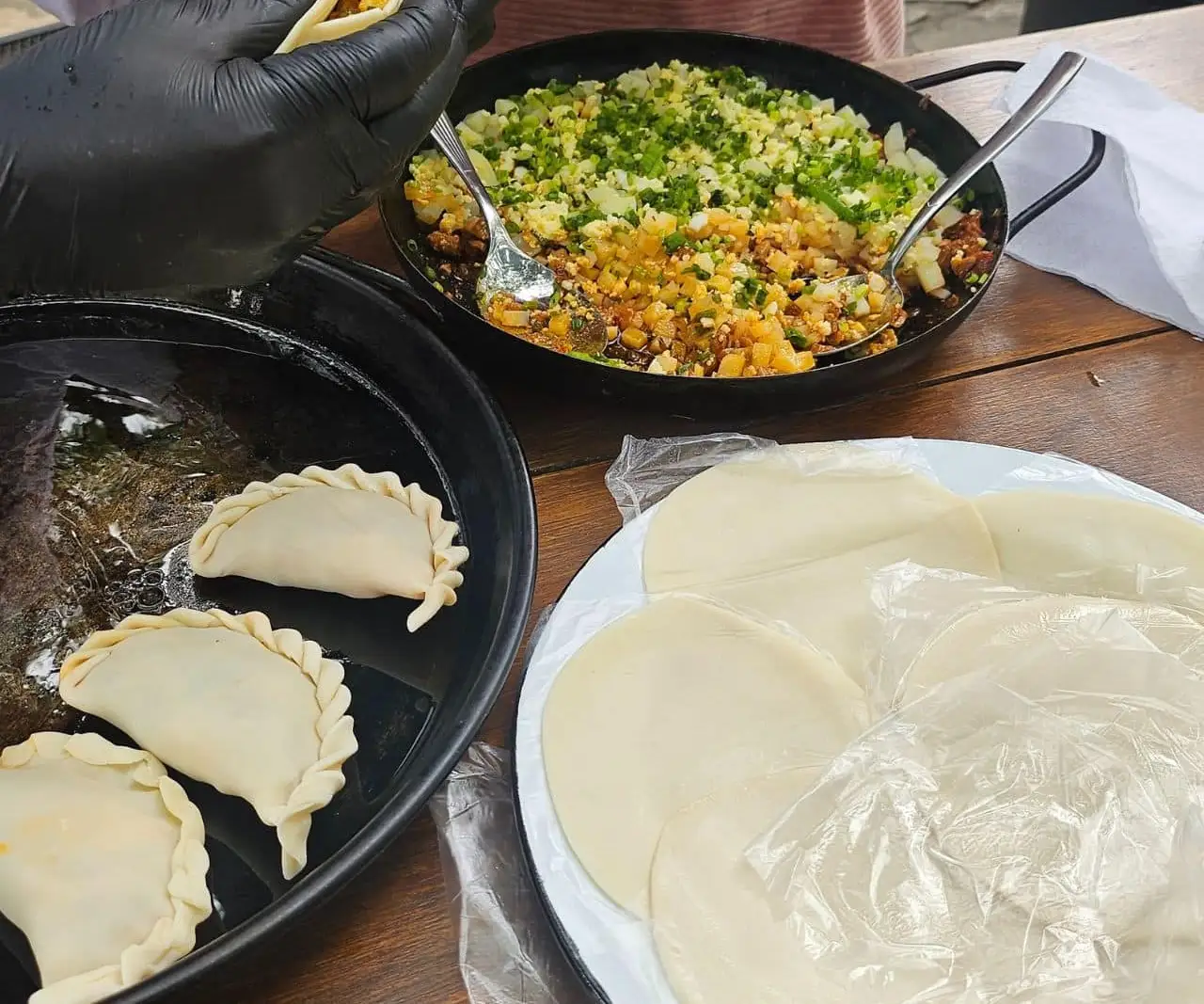 Folded empanadas on a tray, with the pastry discs and a pan of filling