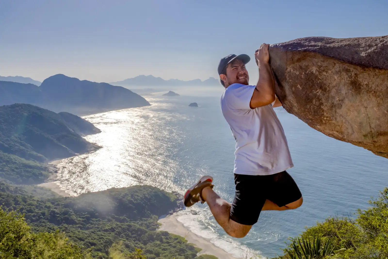 A walker hanging from the rock at Pedra do Telégrafo, above the coast