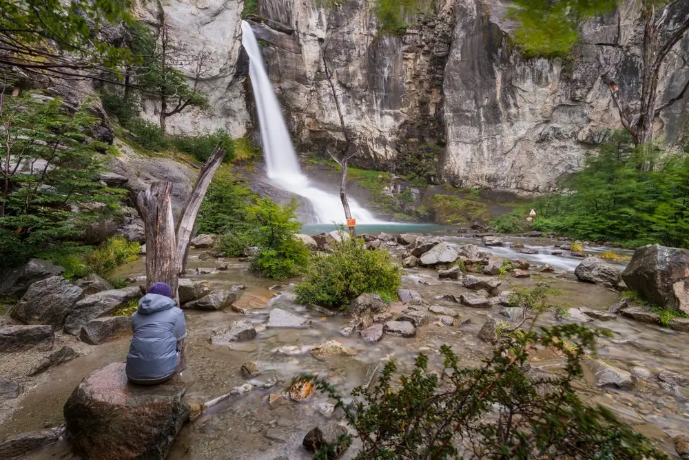 A waterfall in the rocks, with a walker resting below it