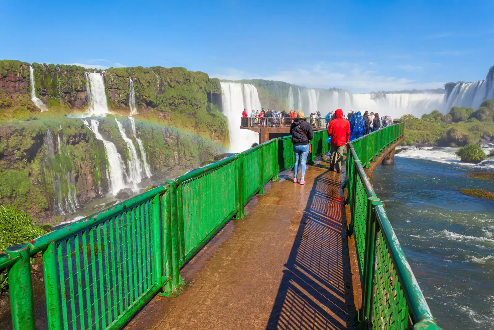 Visitors on the green walkway at the falls, with a rainbow over the water